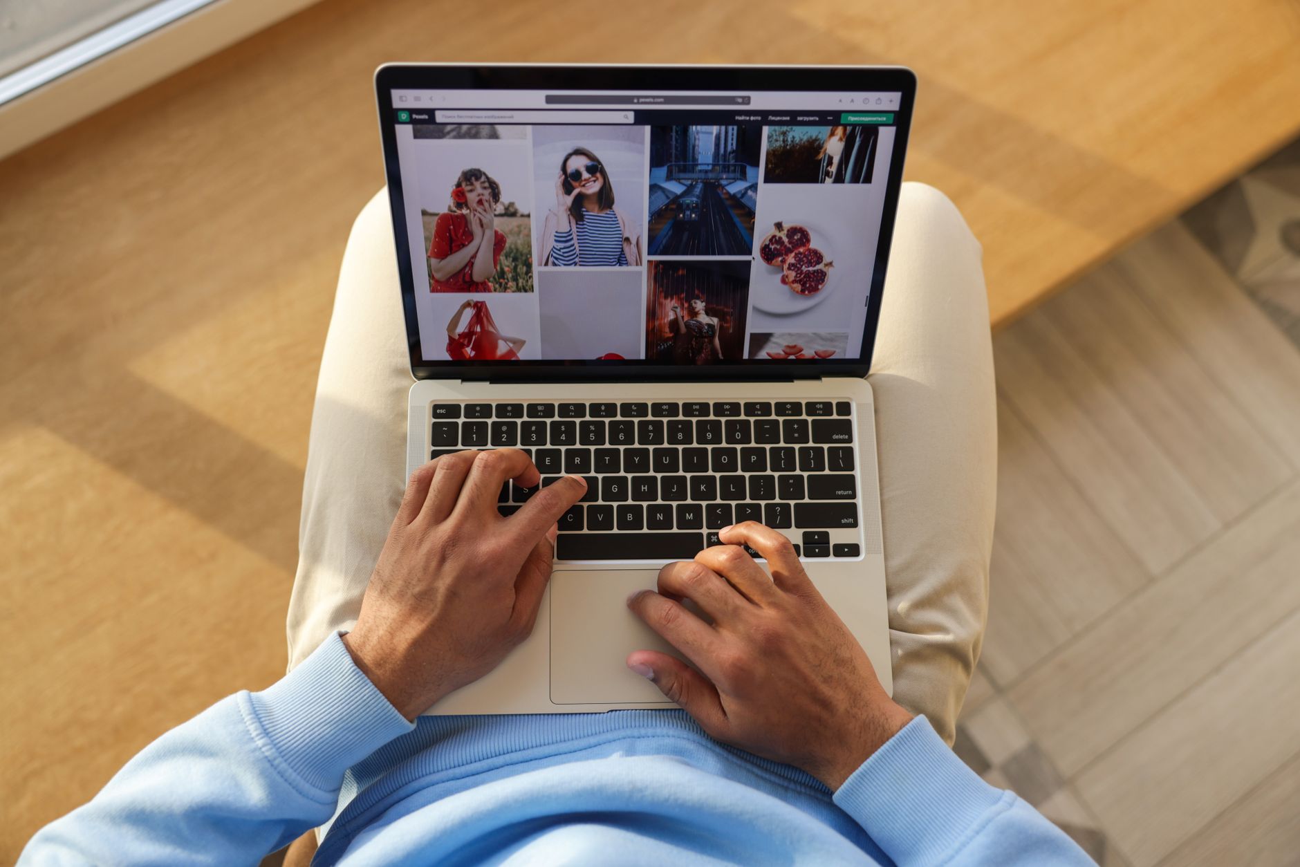 Person mit blauem Hemd bedient Laptop mit Fotogalerie auf hölzernem Tisch
